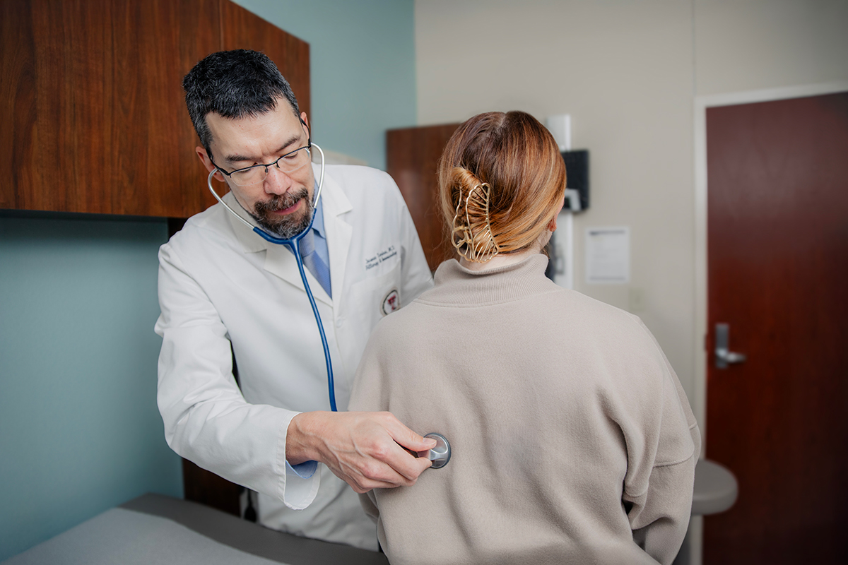 James Tarbox, M.D., with patient in clinic listening to breathing through stethoscope
