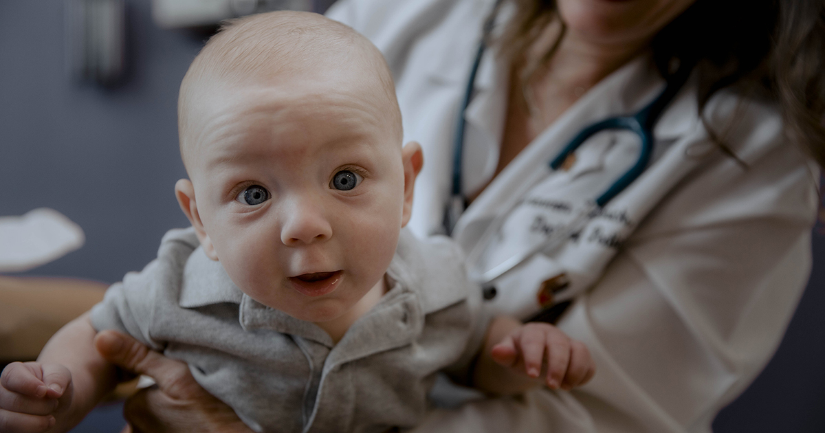 cute baby with a wonderous expression gazes at the camera while being held by his doctor