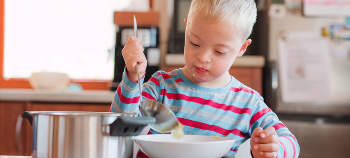 Child holding a spoon over a bowl in a kitchen