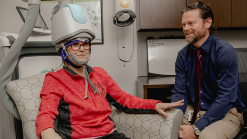 Provider sitting in front of patient in clinic room with medical equipment on head.